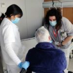 Una enfermera del HSJD enseña a una auxiliar de Enfermería en prácticas el procedimiento con un paciente.
