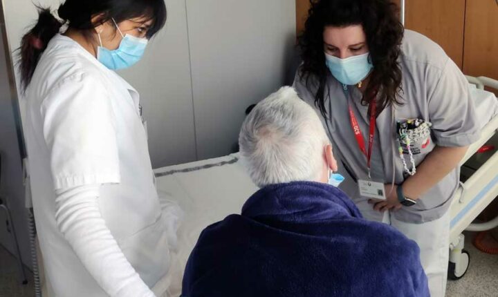 Una enfermera del HSJD enseña a una auxiliar de Enfermería en prácticas el procedimiento con un paciente.